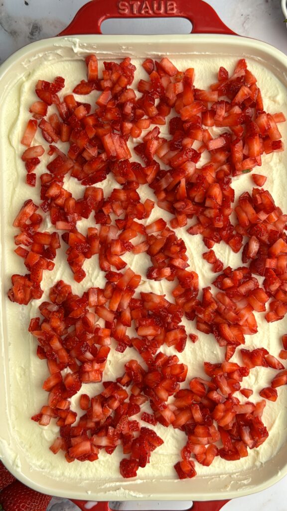 chopped strawberries over white cream in a baking dish. The inside of a cake.