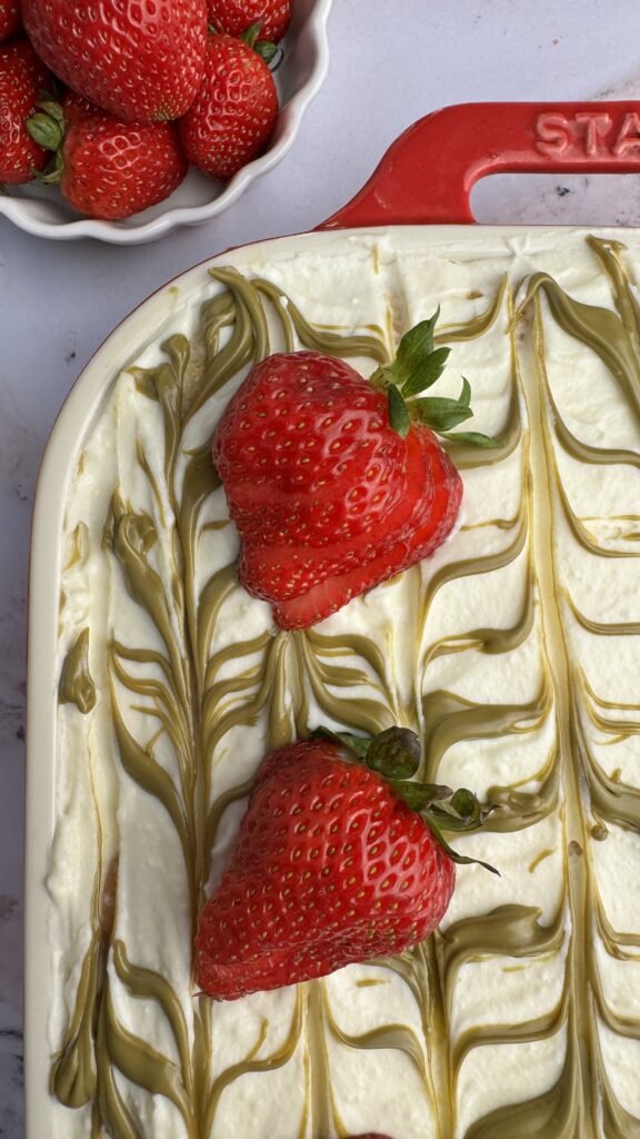 close up of strawberry pistachio tiramisu decorated with white cream topped with pistachio cream lines and whole strawberries.